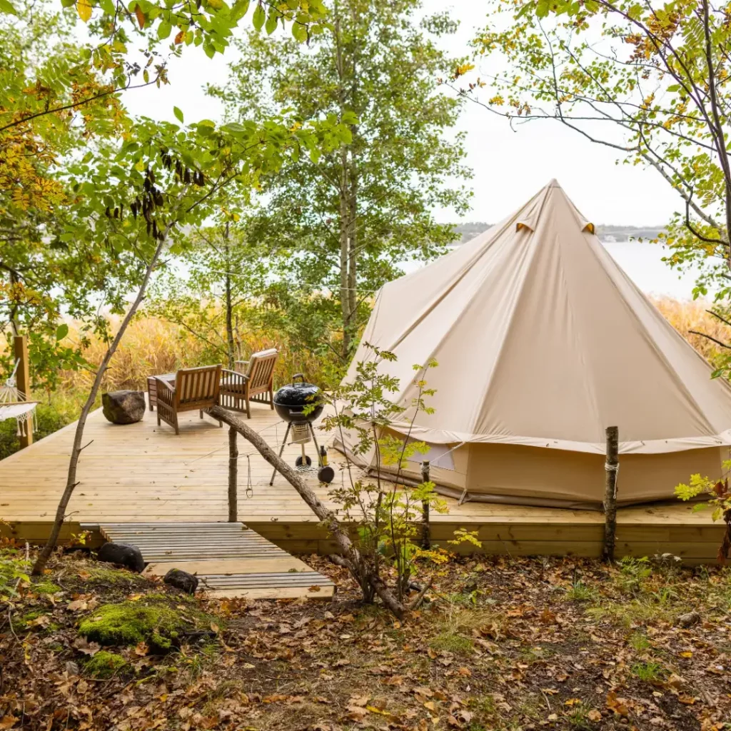 Glampingtält på en trall, havsutsikt en hängmatta, två fåtöljer, havet och grönskan.