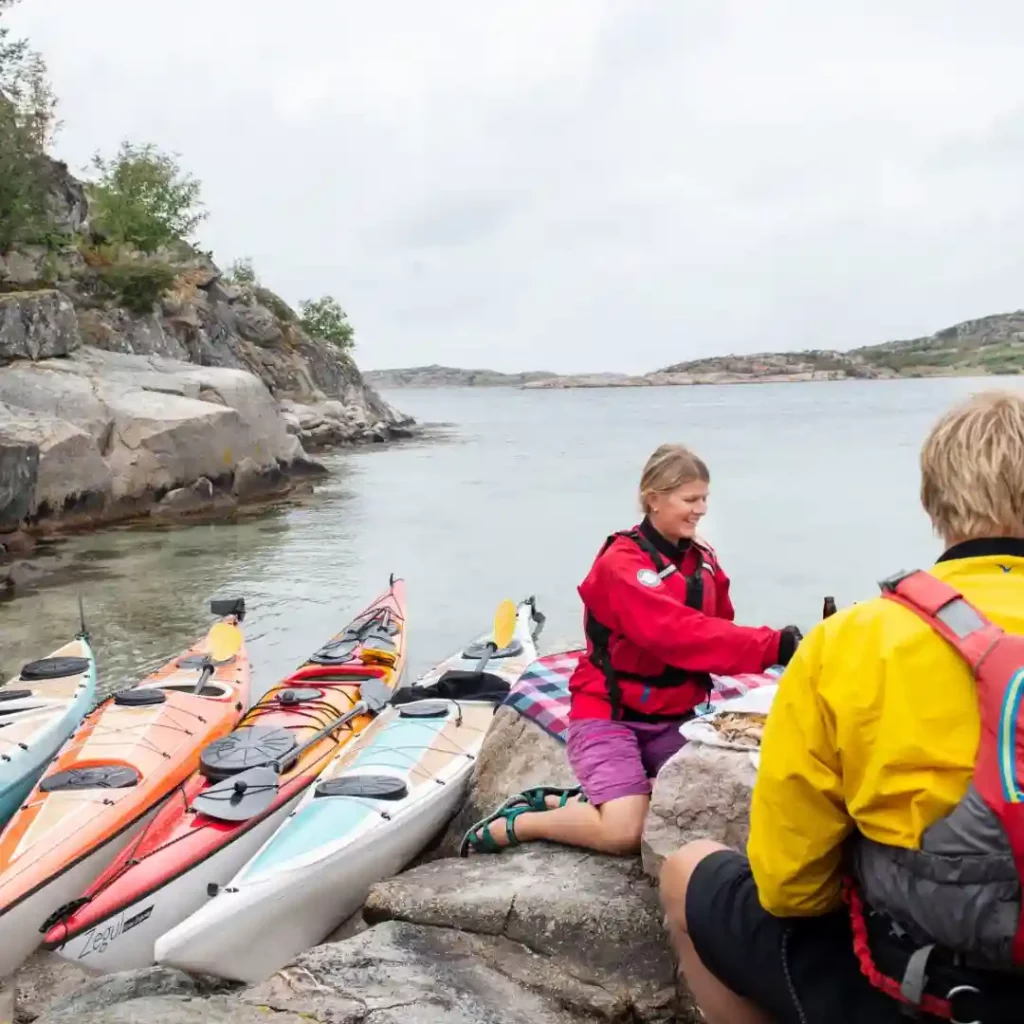 Mänisskor som har picknick på en kobbe med kajakerna i Bohuslän